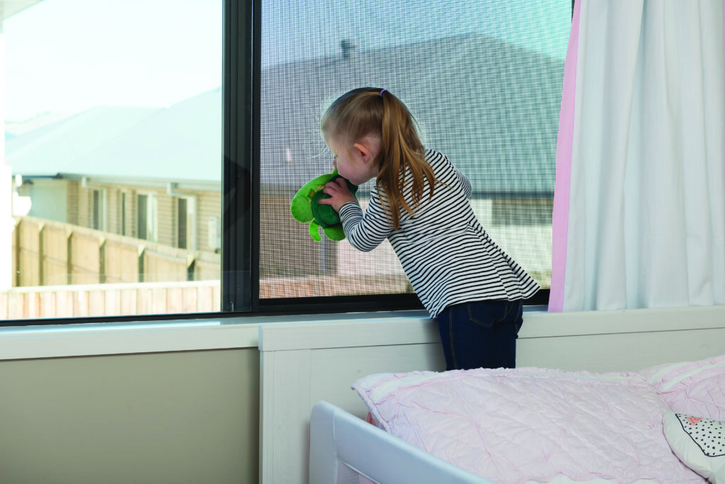 Little girl standing by the window with Guardian Fall Safe Screens